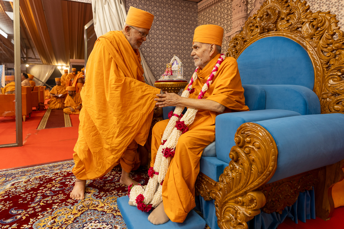 Pujya Ghanshyamcharan Swami honors Swamishri with a garland